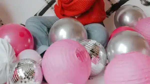 persona con jersey rojo rodeada de bolas de discoteca plateadas y globos rosas