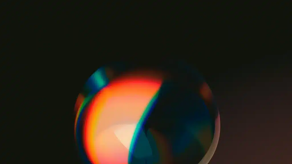 An abstract image featuring a colorful reflection on a transparent sphere set against a dark background, showcasing a blend of bright orange, red, and blue hues.