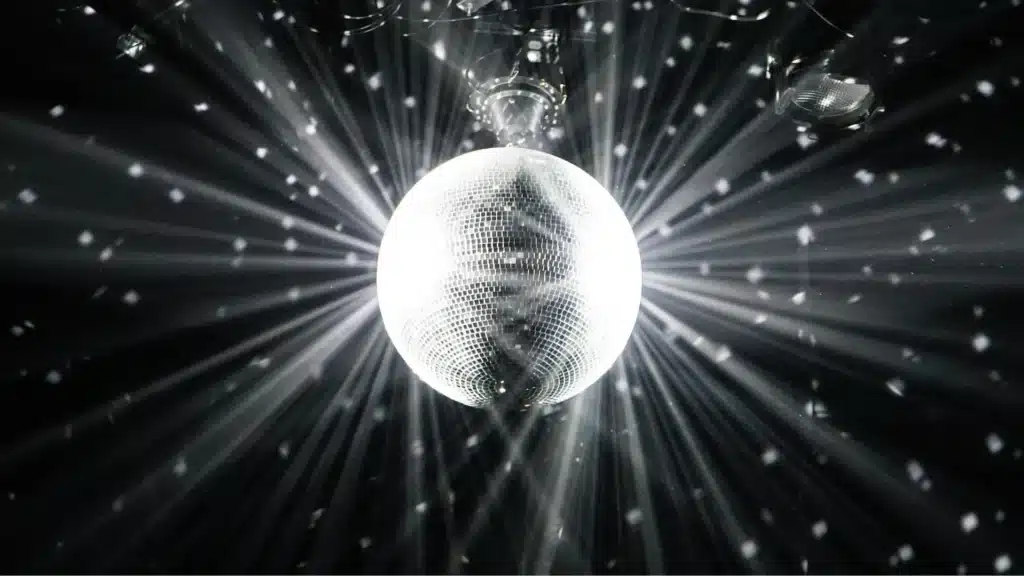 A disco ball hanging from the ceiling shines bright light patterns across a dark room.