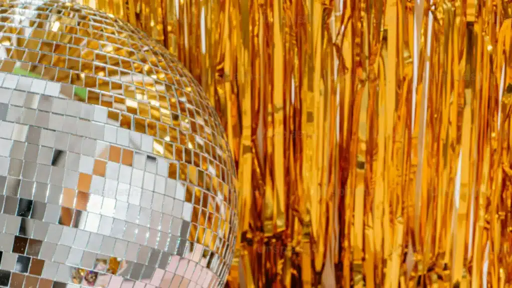 Una bola de discoteca que refleja la luz con un telón de fondo de brillantes serpentinas doradas.