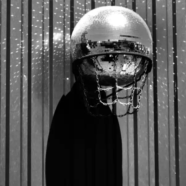 Una bola de discoteca colocada de forma creativa dentro de una canasta de baloncesto cuyo reflejo proyecta dibujos sobre una pared a rayas.