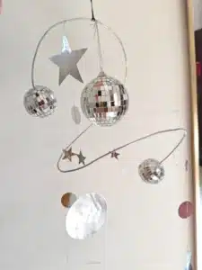 A decorative mobile featuring two disco balls, stars, and round shapes suspended from metal wires, against a plain background.