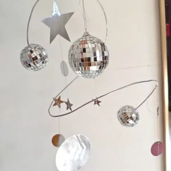 Móvil decorativo con dos bolas de discoteca, estrellas y formas redondas suspendidas de alambres metálicos, sobre un fondo liso.