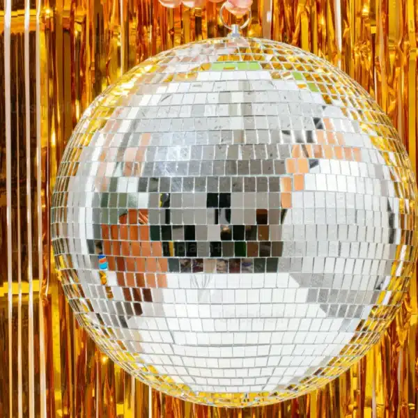 Una brillante bola de discoteca colgando delante de adornos de espumillón dorado.