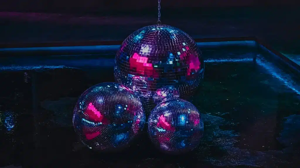 Multiple disco balls reflecting blue and pink neon lights in a dark room.