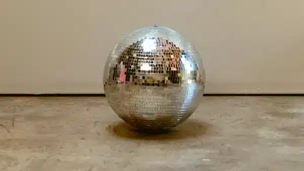 Una brillante bola de discoteca plateada colocada en un suelo de cemento contra una pared lisa.