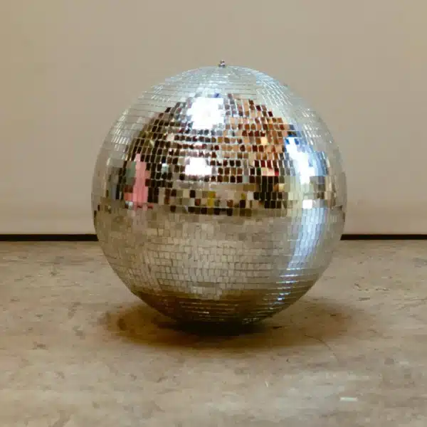 Una brillante bola de discoteca plateada colocada en un suelo de cemento contra una pared lisa.