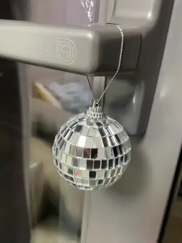 Primer plano de una minibola de discoteca que cuelga de la manilla metálica de una puerta y refleja la luz en varias direcciones.