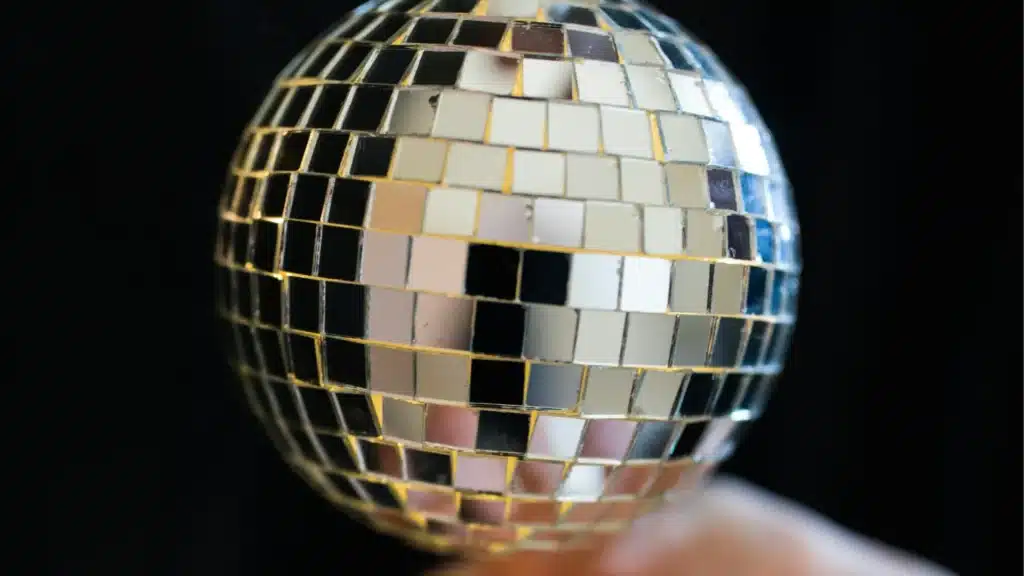 Primer plano de una bola de discoteca con azulejos cuadrados reflectantes sobre fondo negro.