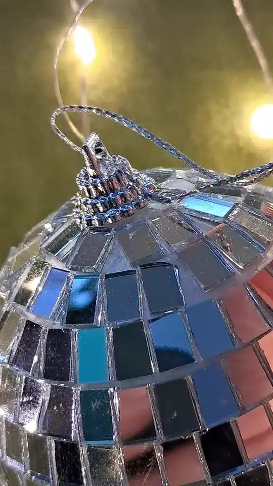 Primer plano de un adorno de bola de espejos con pequeños azulejos reflectantes, con luces borrosas de fondo.
