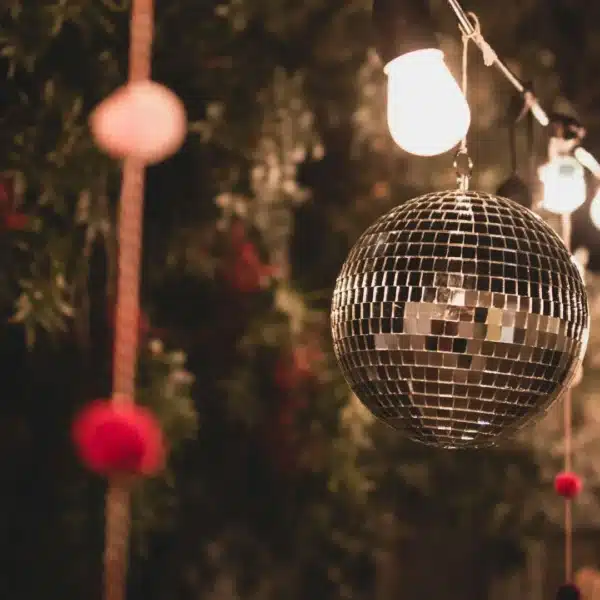 Una bola de discoteca colgada en el exterior con luces de cuerda y elementos decorativos, creando un ambiente festivo.