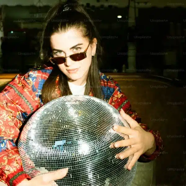 Persona con gafas de sol y chaqueta de colores sosteniendo una gran bola de discoteca