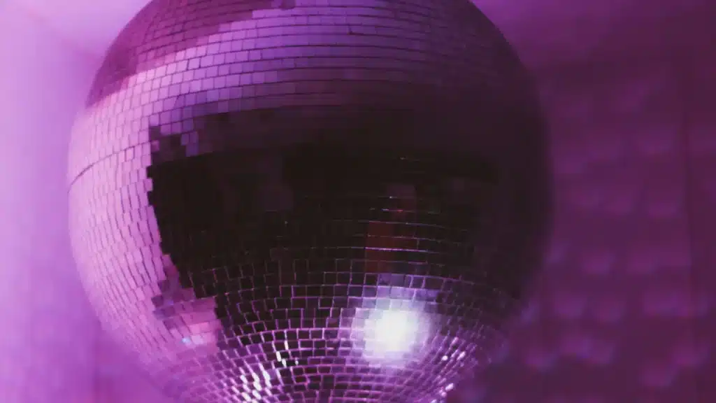 A disco ball reflecting pink and purple light in a dimly lit room.