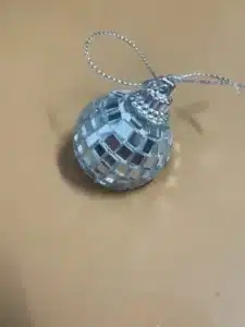 A small reflective disco ball ornament with a metallic loop on a beige surface.