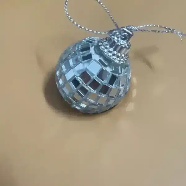 Pequeño adorno de bola de discoteca reflectante con un lazo metálico sobre una superficie beige.